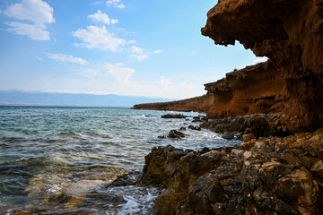 Ocean waves crashing on a rocky shore with a large rock formation in the foreground and blue sky