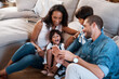 © Chanelle2000/peopleimages.com - Kids, parents and happy family with phone for video call, game and laughing in home together. Children, father and mother with mobile for funny movie, learning or interracial people relax in lounge
