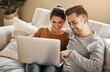 © Chanelle2000/peopleimages.com - Couple, relax and laptop on sofa for website, streaming and family video call in home. Man, happy woman and computer in living room for connectivity, love and tech for communication or choosing media