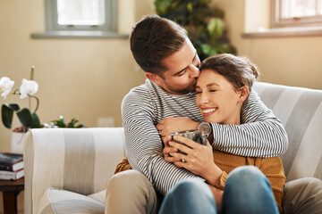 Wall Mural - Home, couple and kiss on forehead for love, support and bonding together in marriage. Happy people, woman and man with hug embrace for admiration, commitment and affection with coffee cup on sofa