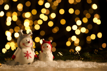 Wall Mural - Cute decorative snowmen on artificial snow against blurred lights. Space for text