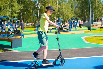 12 year old boy riding scooter on bike path in park in summer