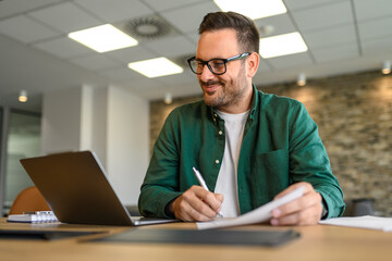 Wall Mural - portrait of financial analyst examining report and working on new strategies over laptop in office