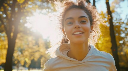 Sticker - A woman with curly hair is smiling in the sun. She is wearing a hoodie and is running in a park