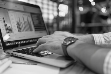 Canvas Print - A man is typing on a laptop computer. The laptop is open to a screen with a lot of graphs and numbers. The man is wearing a watch and he is focused on his work