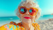 © Sana Sabina - Selfie photo of an elderly female blogger in bright sunglasses and bright clothes, on the beach background.