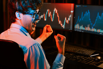 Successful business trader raising fist up with highest profit looking on global market online in real time at neon light modern office. Concept of dynamic stock exchange young businessman. Gusher.