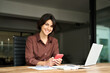 © insta_photos - Happy young Hispanic business woman executive looking at camera holding mobile phone. Smiling female manager or entrepreneur using smartphone tech sitting in office at work, portrait.