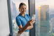 © Yaroslav Astakhov - A professional woman happily engages with her smartphone in a sleek office space overlooking the city.