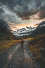 Wall Mural - A lone individual walks along a dirt road surrounded by majestic mountains, suitable for use as a travel or adventure scene