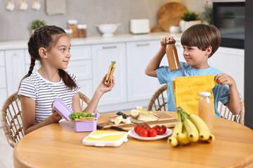 Wall Mural - Cute children with healthy snacks preparing lunch box at wooden table in kitchen