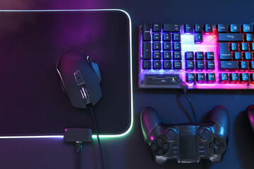 Wall Mural - Computer mouse, RGB keyboard and game controller in neon lights on dark background, flat lay