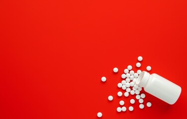 White Pill Bottle with Small Round Pills Spilling Out on a Red Background