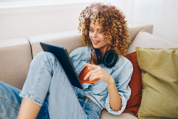 Wall Mural - Happy Woman Holding Tablet PC and Listening to Music, Relaxing on Couch at Home