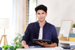 © mangpor2004 - Portrait of happy young business man owner holding digital tablet smiling and looking at camera while sitting at home office