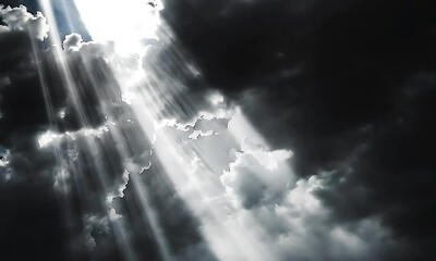 sunlight breaks through thick dark clouds, creating dramatic light beams in a moody sky.