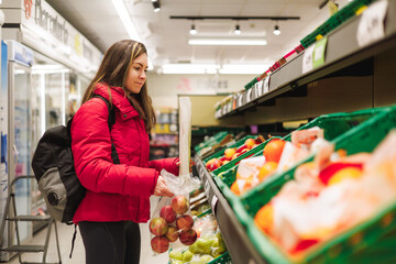 Latin woman with red coat choosing fruits in supermarket.