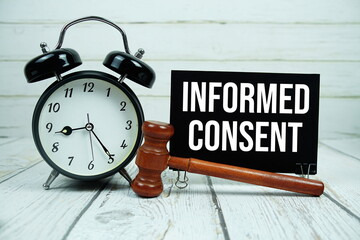 Informed Consent text on paper card with alarm clock and wooden judge gavel on wooden background