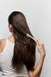 © SHOTPRIME STUDIO - Hair Care, Long Hair, Comb, Back View, Woman, Hair Styling, Healthy Hair, Hair Treatment, Personal Care, Beauty Routine A woman is grooming her long hair with a white comb, showcasing healthy, shiny