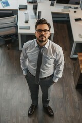 Wall Mural - A man wearing a white shirt and gray pants stands in front of a desk. He is wearing a tie and glasses