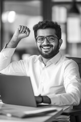 Wall Mural - A man is sitting at a desk with a laptop in front of him. He is smiling and holding his hands up in the air. Concept of happiness and positivity