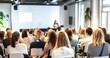© 为轩 张 - Audience view from behind in a conference room with a white wall, watching a speaker and presentation screen. Scandinavian design style with varied colored attire and some attendees sitting back