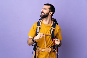 Wall Mural - Caucasian handsome man with backpack and trekking poles over isolated background thinking an idea while looking up