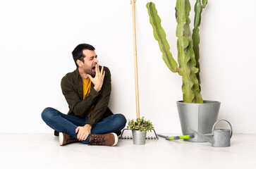 Wall Mural - Gardener man sitting on the floor at indoors yawning and covering wide open mouth with hand