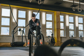 Wall Mural - Young man training with battle ropes at gym