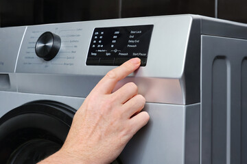 Close-up of hand a adult man press button start automatic washing program switch on the washing machine panel.