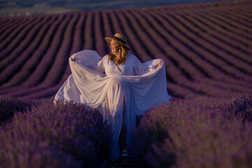 Canvas Print - woman poses in lavender field at sunset. Happy woman in white dress holds lavender bouquet. Aromatherapy concept, lavender oil, photo session in lavender