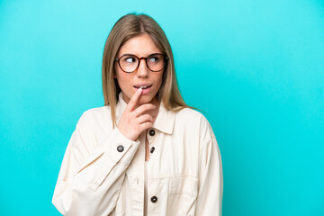 Wall Mural - Young caucasian woman isolated on blue background With glasses and having doubts