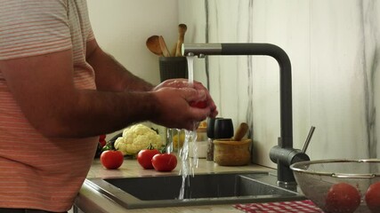 Wall Mural - Man is washing tomato under the tap in the kitchen