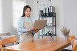 © PRIME STOCK LAB - Asian woman in apron smiles while browsing a recipe on laptop in the kitchen, preparing to cook a meal.