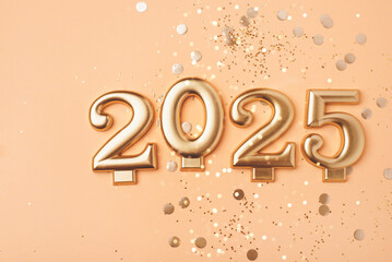 Golden 2025 on a peach color background with confetti and bokeh lights. Happy New Year 2025 is coming concept. Top view.