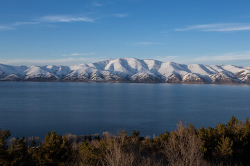 snow capped mountains on lake sevan in clear weather at sunset