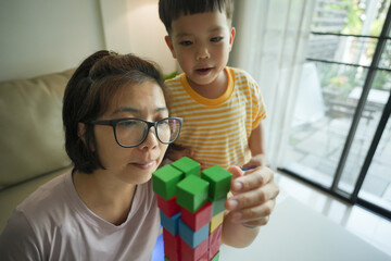 Wall Mural - Asian Mother and child boy stacking colorful building blocks indoors. Home activity for creativity and learning. Playtime and education concept