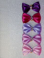 Wall Mural - Pink, purple, fuchsia and indigo bows with a stone in the middle lie on a gray shiny background. many bright beautiful bows. pet accessories. top view. five bows, copy space