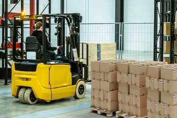 Wall Mural - Warehouse distribution center. Forklift drives around storage hangar. Factory warehouse area with boxes. Forklift moves pallets with parcels. Industrial warehouse. Modern distribution hub