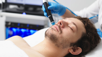 Facial skin care. A professional female cosmetologist performs a hydraulic procedure on a man in a cosmetology clinic. Vacuum cleaner Hydra. Rejuvenation and hydration