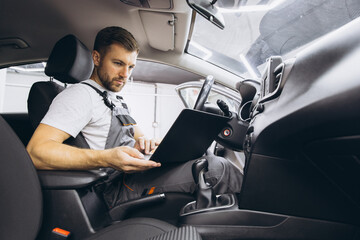 Wall Mural - Automotive mechanic running diagnostics software on computer. Mechanic sitting in car and working on laptop while doing vehicle diagnostic test in auto service garage.