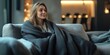 © Valerii Dekhtiarenko - Woman peacefully sitting on a couch, wrapped in a dark blanket, enjoying a calm moment in a minimalist living room