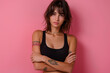 © Sascha - Fashionable female model with stylish tattoo wearing black tank top standing in front of a pink wall. Trendy brunette lady posing for a studio portrait.