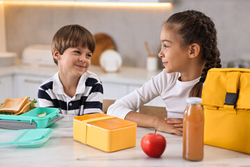 Wall Mural - Cute children preparing school lunch boxes with healthy food at white marble table in kitchen