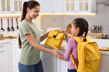 Canvas Print - Smiling mother giving lunch bag to her daughter in kitchen. Preparing for school