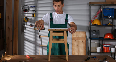 Wall Mural - Man using tape measure while repairing wooden stool indoors