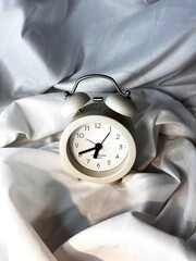 White vintage alarm clock on white textile background