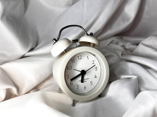 White vintage alarm clock on white textile background