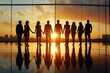 © Rattadet - Silhouettes of diverse professionals holding hands against a vibrant sunset, symbolizing unity and collaboration in the workplace.