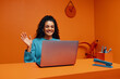 © Jacob Lund - Female remote worker waving while working on laptop in vibrant orange office